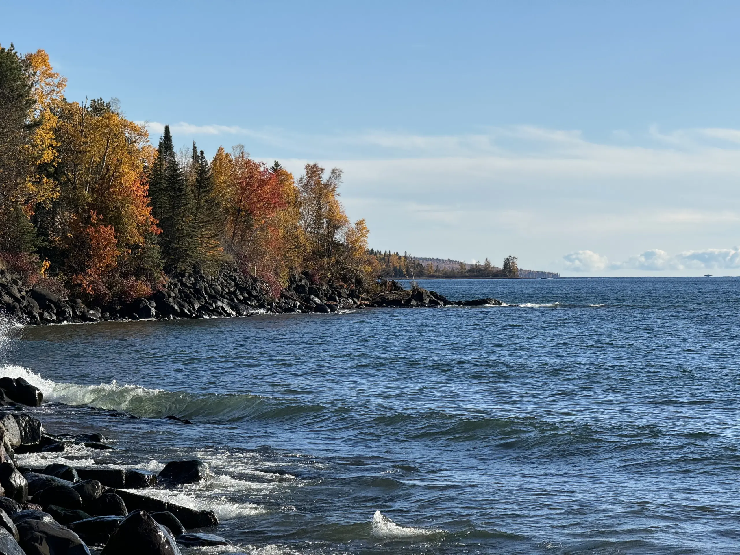 Autumn trees along a rocky lakeshore beneath a blue sky.